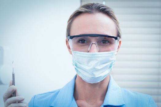 Portrait of female dentist in surgical mask and safety glasses holding injection