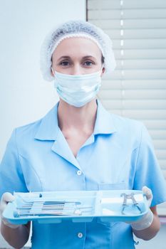 Portrait of female dentist in surgical mask holding tray of tools