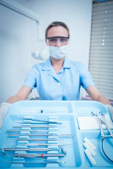 Portrait of female dentist in surgical mask holding tray of tools