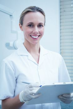 Portrait of smiling young female dentist holding clipboard