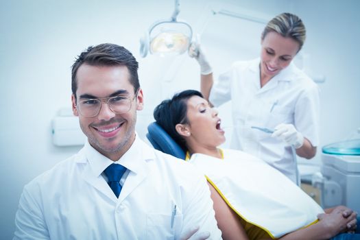 Portrait of smiling male dentist with assistant examining womans teeth in the dentists chair