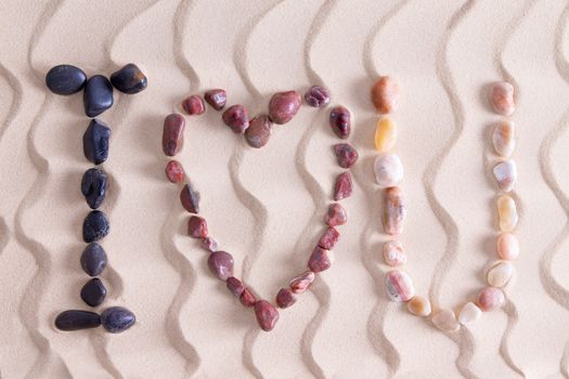 I Love You romantic message in colorful pebbles on golden beach sand with a decorative pattern of undulating wavy lines using waterworn basalt, agate and quartzite found in nature on the seashore