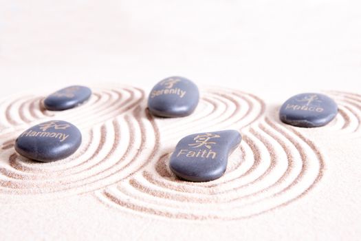 Zen art with swirling lines in golden sand surrounding smooth basalt rocks with symbols and text signifying peace, harmony, hope, belief, and serenity in ancient Japanese tradition