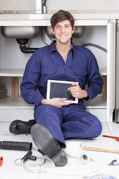 Happy plumber sitting on the floor holding his tablet