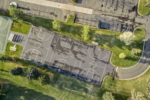 aerial view of a public park with recreational basketball courts and parking lot, sunrise light with long shadows at springtime