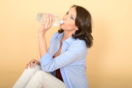 Beautiful Young Woman Sitting on the Floor Wearing a Blue Shirt and White Jeans Smiling Holding A Bottle of Still Mineral Water.