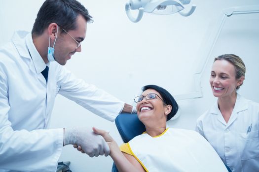 Male dentist shaking hands with woman in the dentists chair