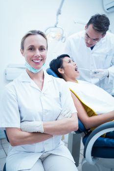 Portrait of smiling female dentist with assistant examining womans teeth in the dentists chair