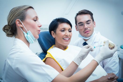 Female dentist with assistant showing woman how to brush teeth in the dentists chair