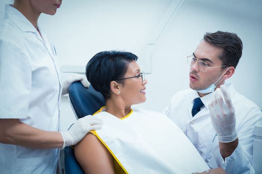 Male dentist with assistant examining womans teeth in the dentists chair