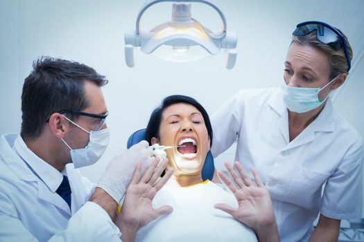 Male dentist with assistant examining womans teeth in the dentists chair