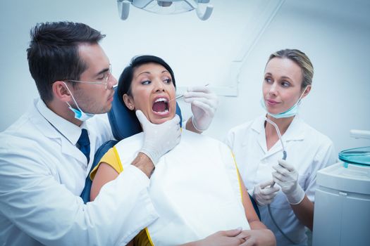 Male dentist with assistant examining womans teeth in the dentists chair