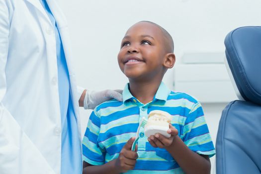 Cropped dentist teaching young boy how to brush teeth