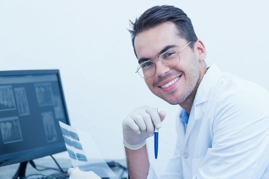 Portrait of smiling male dentist with x-ray on computer