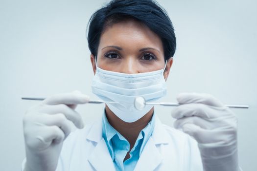 Portrait of female dentist in surgical mask holding dental tools