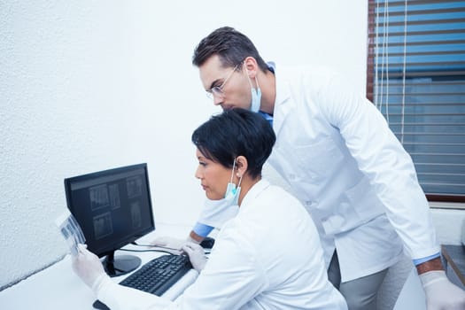 Side view of concentrated dentists looking at x-ray on computer