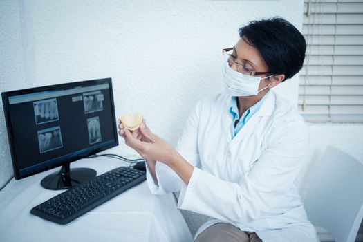 Female dentist wearing surgical mask while holding mouth model