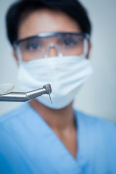 Portrait of female dentist in surgical mask holding dental drill