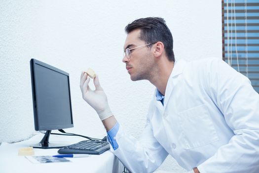 Male dentist holding mouth model besides computer