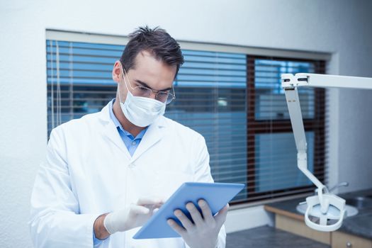 Concentrated male dentist in surgical mask using digital tablet