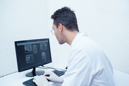 Side view of concentrated male dentist looking at x-ray on computer