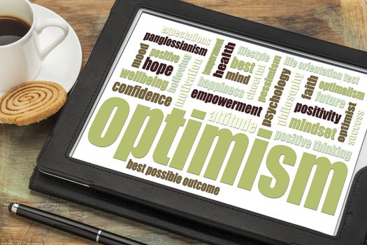 optimism word cloud on a digital tablet with a cup of coffee