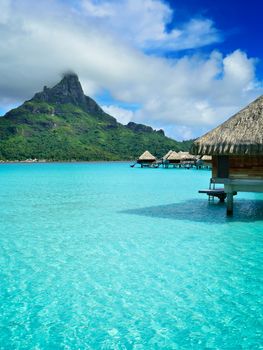 Luxury overwater honeymoon bungalows in a vacation resort in the clear blue lagoon with a view on Mt. Otemanu on the tropical island of Bora Bora, near Tahiti, in French Polynesia.