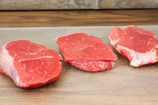 Fresh beef steaks on a clear cutting board resting on a counter top.