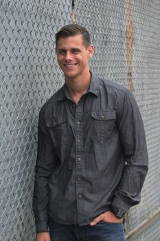 Portrait of a man standing in front of a chain link fence.