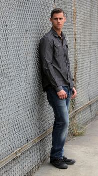 Portrait of a man standing in front of a chain link fence.