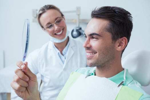 Smiling young man looking at mirror in the dentists chair