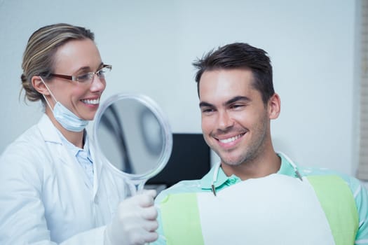 Smiling young man looking at mirror in the dentists chair