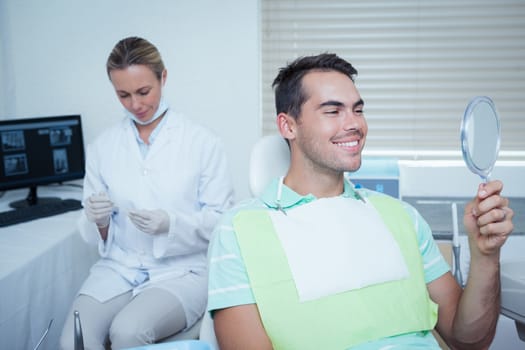 Smiling young man looking at mirror in the dentists chair