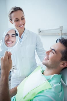 Smiling young man looking at mirror in the dentists chair