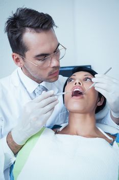 Male dentist examining womans teeth in the dentists chair