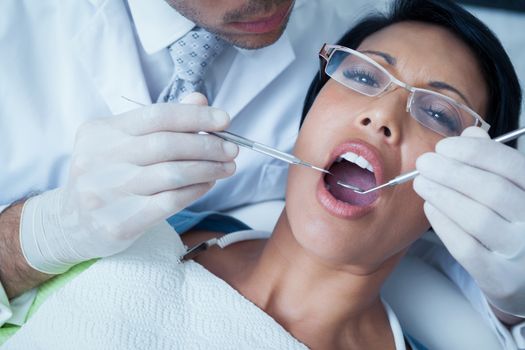 Male dentist examining womans teeth in the dentists chair