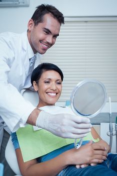 Smiling young woman looking at mirror in the dentists chair