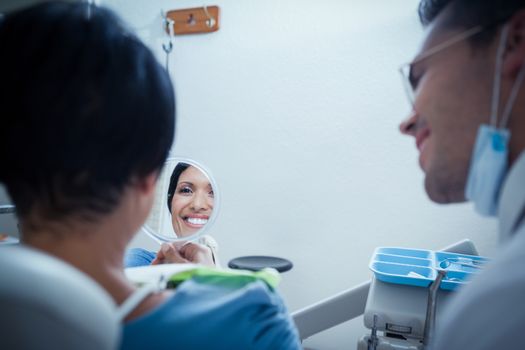 Smiling young woman looking at mirror in the dentists chair