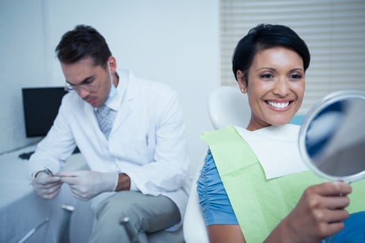 Smiling young woman looking at mirror in the dentists chair