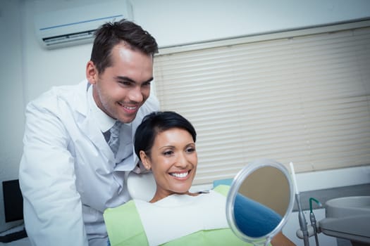 Smiling young woman looking at mirror in the dentists chair