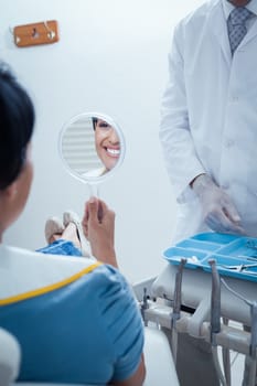 Smiling young woman looking at mirror in the dentists chair