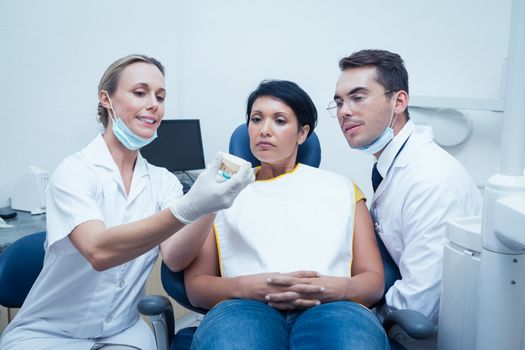 Female dentist with assistant showing woman prosthesis teeth