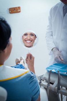 Smiling young woman looking at mirror in the dentists chair