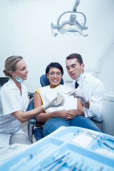 Female dentist with assistant showing woman prosthesis teeth