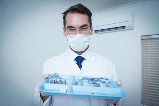 Portrait of male dentist in surgical mask holding tray of tools