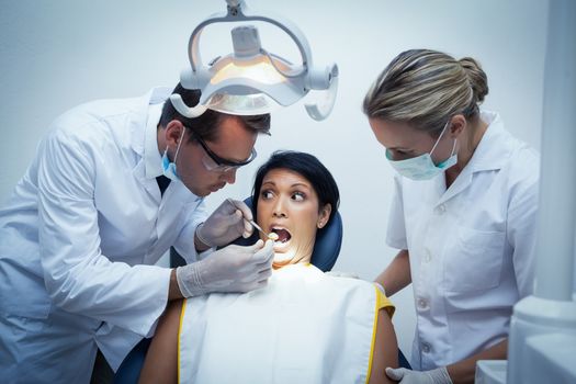 Male dentist with assistant examining womans teeth in the dentists chair