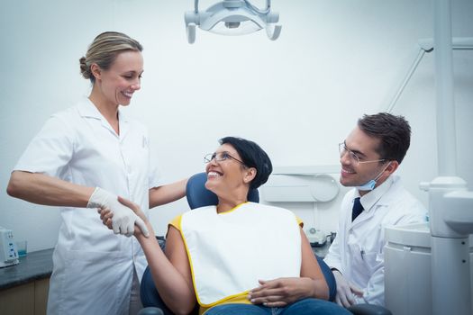 Male dentist with assistant shaking hands with woman in the dentists chair