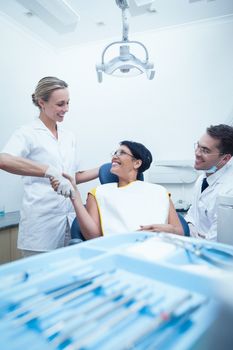 Male dentist with assistant shaking hands with woman in the dentists chair