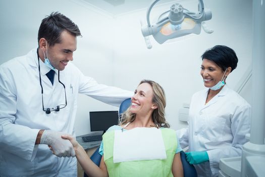Male dentist with assistant shaking hands with woman in the dentists chair