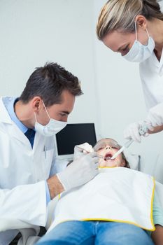 Male dentist  with assistant examining girls teeth in the dentists chair